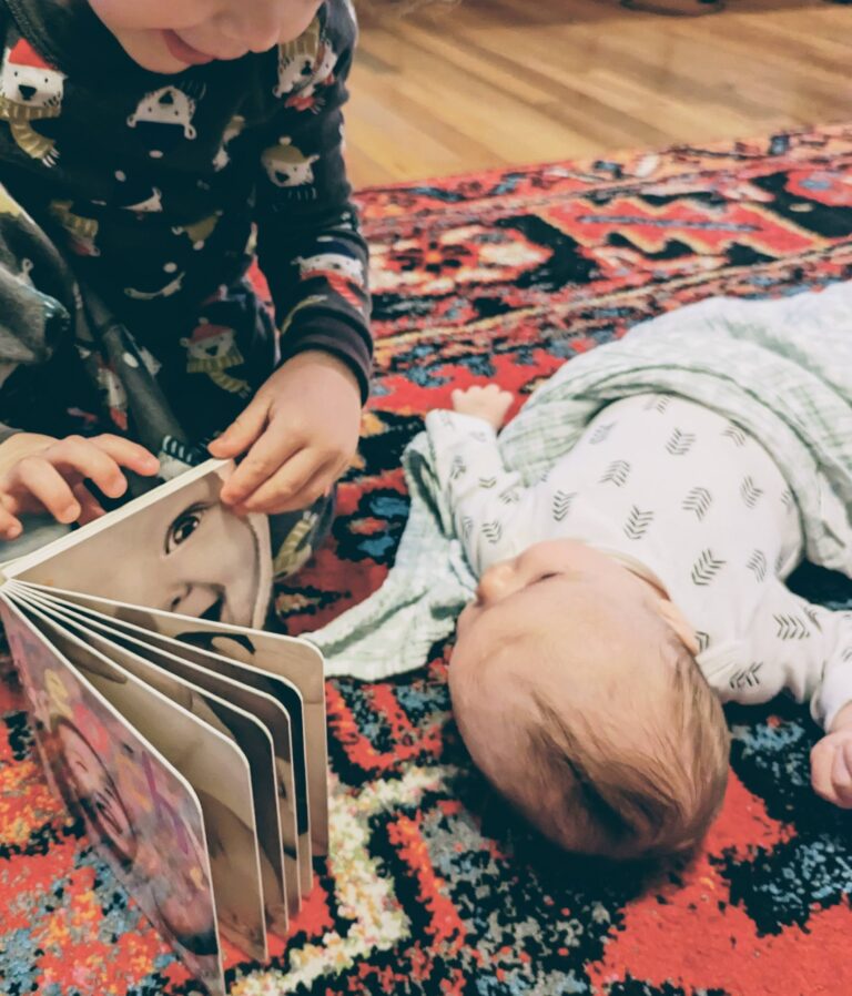 toddler reading book to newborn